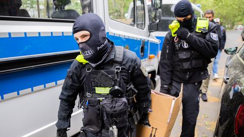 Zwei Polizisten tragen einen Umzugskarton zu einem Fahrzeug.