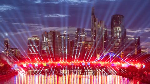 Scheinwerfer leuchten von einer Brücke in der Frankfurter Innenstadt, die Skyline wird angestrahlt.