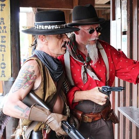 Zwei Cowboys, einer mit Waffe, stehen vor einer Tür.