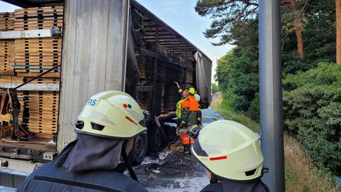 Feuerwehrleute betrachten einen Lkw-Anhänger, auf dem Holz gebrannt hat.