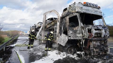 Ein ausgebrannter Lkw wird von zwei Feuerwehrleuten gelöscht