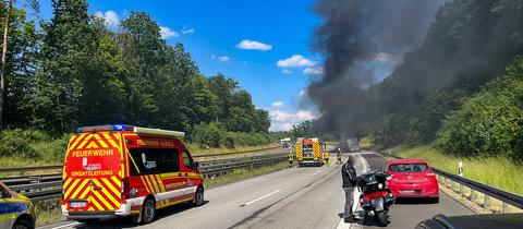 Rauch steigt aus brennendem Lkw auf Autobahn, Rettungskräfte vor Ort