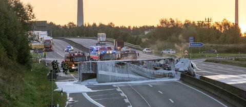 Ausgebranntes Lkw-Gerippe in Löschschaum querliegend auf Autobahn mit Feuerwehrwagen