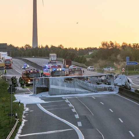 Ausgebranntes Lkw-Gerippe in Löschschaum querliegend auf Autobahn mit Feuerwehrwagen