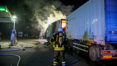 Feuerwehrleute löschen einen brennenden Lkw auf einem Tankstellengelände.