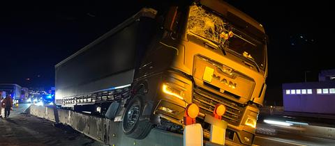 Ein Lkw hängt nach einem Unfall auf einer Autobahn auf einer halbhohen Betonwand.