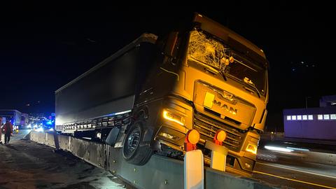 Ein Lkw hängt nach einem Unfall auf einer Autobahn auf einer halbhohen Betonwand.