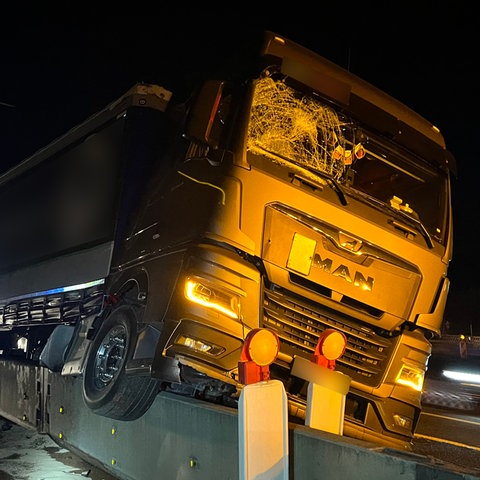 Ein Lkw hängt nach einem Unfall auf einer Autobahn auf einer halbhohen Betonwand.