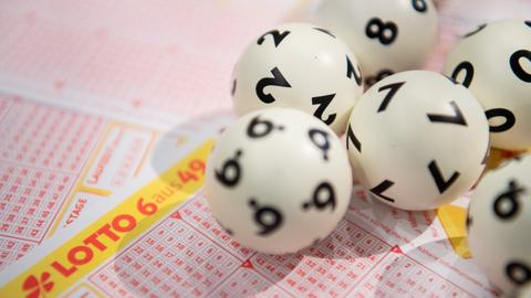 Lottokugeln liegen auf einem Tippschein. 