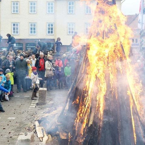 Bildkombination aus zwei Fotos: links eine Kinderhand, die Kastanien hält; rechts eine Foto des Lullusfestes: KInder und Erwachsene stehen um eine großes Feuer herum und werfen Kastanien hinein.