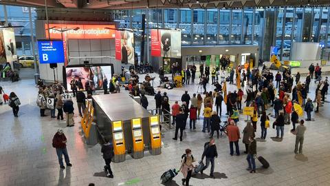 Eine Gruppe von rund 100 Menschen mit Plakaten und Schildern steht bei einer Demonstration in einem Flughafen-Terminal