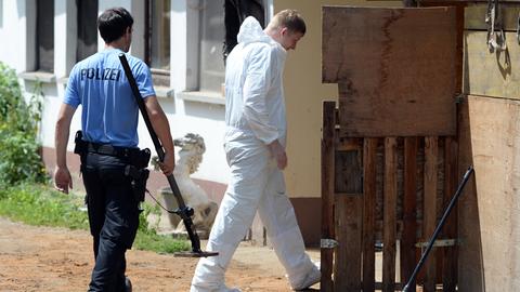 Ein Polizist mit einem Metalldetektor, ein Mann mit weißem Overall der Sprurensicherung.