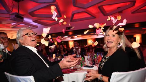 Marianne und Michael sitzen bei einer Gala am Tisch und werfen Rosenblätter in die Höhe.