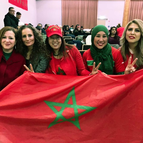 Fünf lachende Frauen, die eine Marokko-Flagge hochhalten.