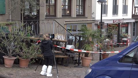 Rot-weißes Absperrband und eine Frau mit Schutzüberzug an den Schuhen vor einem Hauseingang.