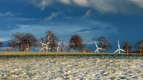 Dunkle Wolken hinter Windrädern. Im Vordergrund Wiese mit etwas Schnee.