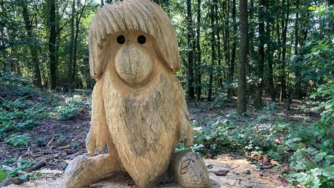 Eine geschnitzte Holzfigur sitzt im Wald auf einem Baumstumpf