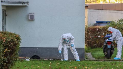 Männer in weißen Schutzanzügen und Handshcuhen suchen den Rasen vor einem Haus nach Spuren ab.