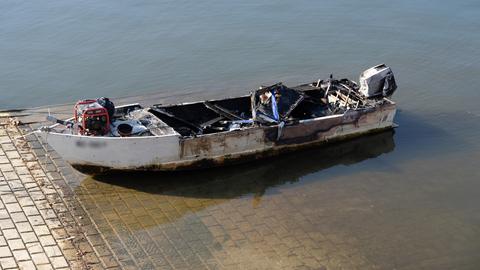 Ein ausgebrannte Motorboot am Ufer einer Wasserfläche.