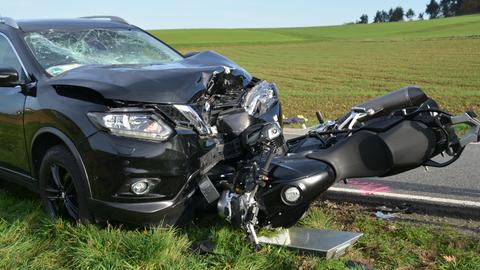 Ein schwarzes Motorrad, das unter einem schwarzen Pkw geraten ist - beide Fahrzeuge sind teils schwer beschädigt.