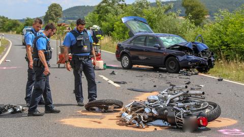 Auf einer Landstraße liegt nach einem Unfall ein stark beschädigtes Motorrad, dahinter steht ein beschädigtes Auto.