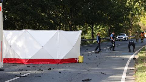 Ein Sichtschutz steht auf einer Straße, Polizeikräfte räumen Trümmerteile auf.