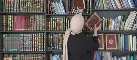Muslima mit Kopftuch steht vor einem Bücherregal