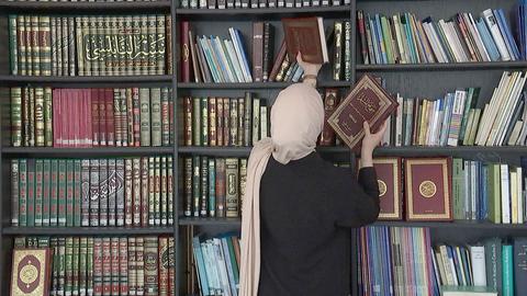 Muslima mit Kopftuch steht vor einem Bücherregal