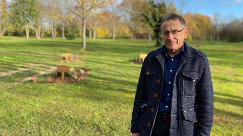 Ein Mann steht auf einem Friedhof und schaut in die Kamera