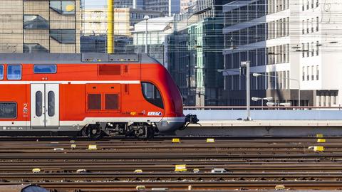 Das Foto zeigt einen Nahverkehrszug vor der Stadtkulisse Frankfurts - eingespannt zwischen Gleislinien und Oberleitungslinien.