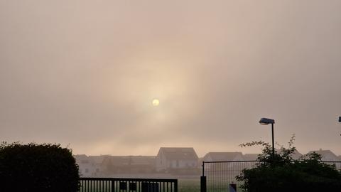 Die Sonne geht im Nebel über einem Wohngebiet auf.