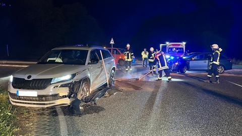 Ein beschädigtes Auto steht auf einer Bundesstraße, dahinter Einsatzkräfte und ein Rettungswagen.