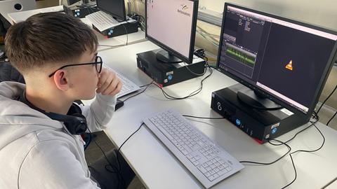 Ein Schüler sitzt vor einen Bildschirm, der ein Audioschnittprogramm zeigt.