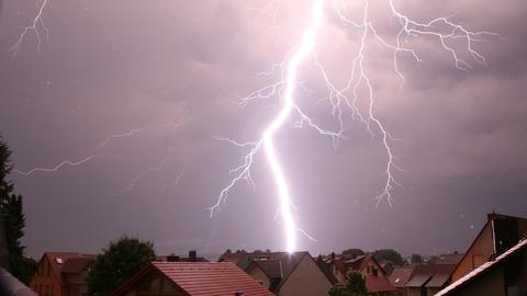 Bei Nacht schlägt ein Blitz über einem Wohngebiet ein.