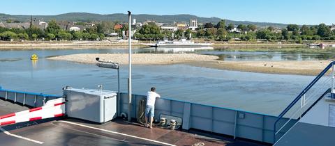 Im Bildvordergrund die Rampe eines Fährschiffes, das ein Flussufer ansteuert. Zwischen Rampe und Flussufer Wasser mit vielen deutlich sichtbaren Sandinseln (Sandbänken).