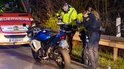 Eine Polizistin und ein Gutachter stehen mit einem Notizblock neben einem Motorrad, im Hintergrund ein Feuerwehrauto. 