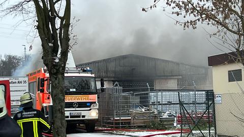 Rauch steigt aus Lagerhalle, Feuerwehrwagen und Einsatzkräfte davor