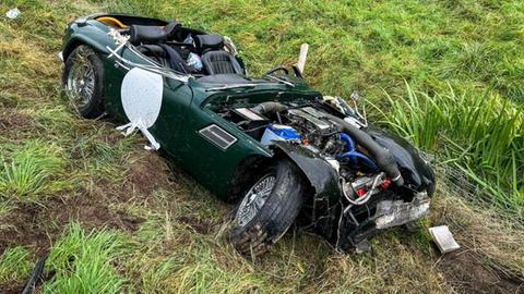 Ein grünes Oldtimer-Fahrzeug steht nach einem Unfall stark beschädigt auf einer Wiese.