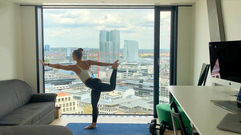 Eine Bewohnerin des sogenannten Omniturms in Frankfurt macht Yoga in ihrer Wohnung - mit Blick auf Frankfurt.