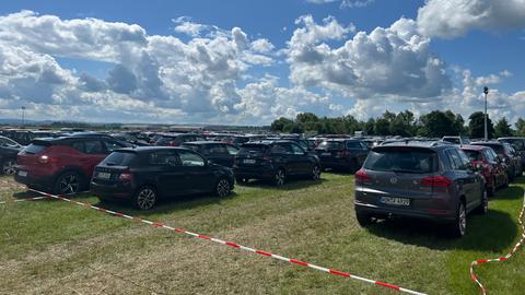 Viele verschiedene Autos stehen eingezäunt von einer Flatterleine auf einem Parkplatz.