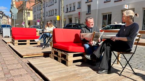 Menschen sitzen auf Sitzmöbeln auf kleinen Holzterrassen, die auf Parkplätzen an der Löherstraße in Fulda stehen. 