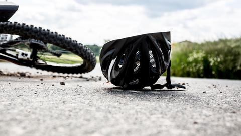 Ein schwarzer Helm liegt neben einem Fahrrad auf der Straße.