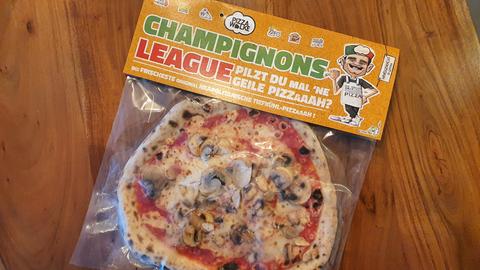 Eine Tiefkühlpizza in einer Plastikverpackung; oben steht groß der Schriftzug Champignons League