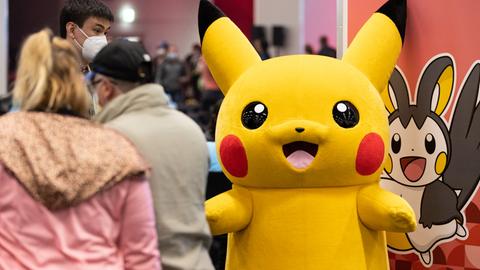 Das Pokémon Pikachu, eine Art stilisierte Maus mit gelbem, weichem Fell, läuft als Maskottchen durch eine Messehalle.