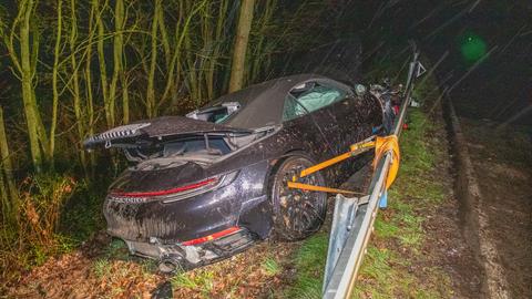 Ein Porsche, der völlig demoliert hinter einer Leitplanke liegt. Das Hinterrad ist mit einem Spanngurt an der Leitplanke fixiert, um nicht am Hang abrutschen. 