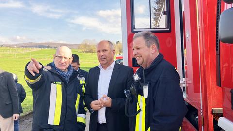 Minister Poseck und Feuerwehrleute stehen neben einem Einsatzfahrzeug der Feuerwehr.