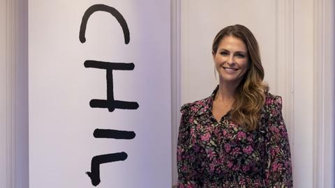 Eine Frau in einem schwarz-rosa gemusterten Kleid steht neben einem Banner mit der Aufschrift "Childhood".