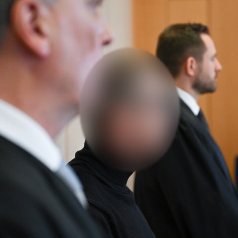 Ein Mann, der gepixelt ist, steht zwischen zwei Männern, seinen Verteidigern, vor Gericht