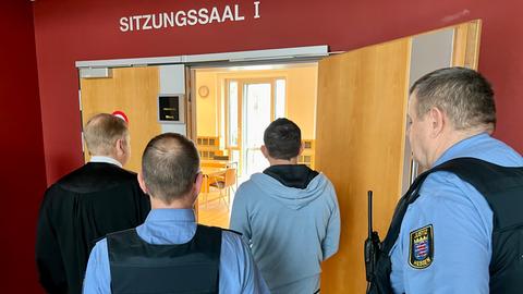 Der Angeklagte und weiteren Menschen betreten im Aschenberg-Prozess einen Sitzungssaal im Landgericht Fulda 