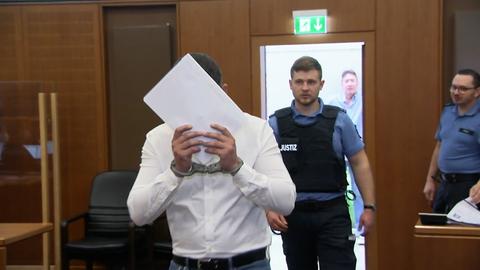 Einer der Angeklagten im Prozess um einen bewaffneten Angriff auf einen Frankfurter Kiosk bedeckt sein Gesicht mit einem Papierblatt, während er den Gerichtssaal betritt.
